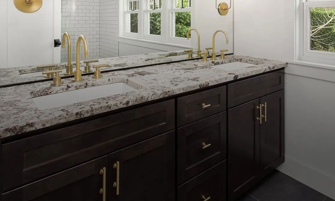 Modern bathroom vanity with dark cabinets, speckled white countertop, gold faucets, and large mirror