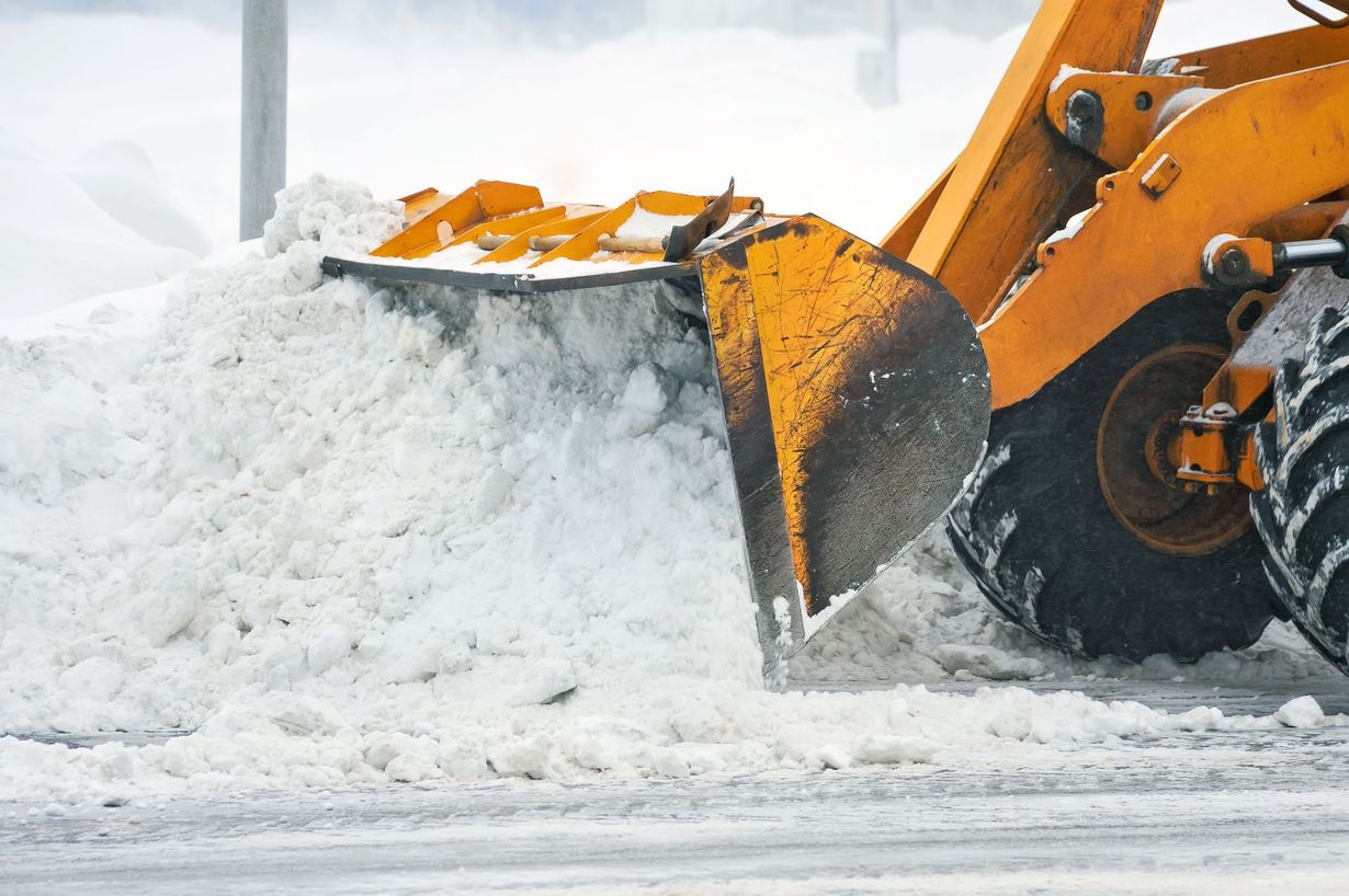 Yellow snowplow clearing snow from a road. The plow is full, and the tires are visible.