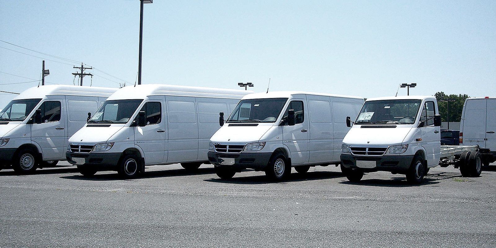 A row of white vans are parked in a gravel lot