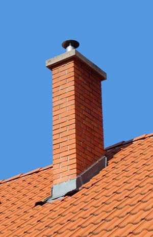 Red brick chimney on a tiled roof against a clear blue sky
