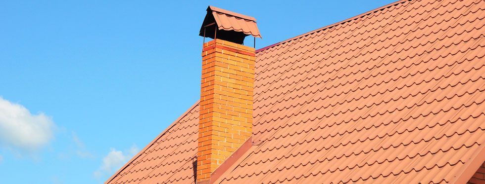Red tiled roof with a brick chimney against a blue sky