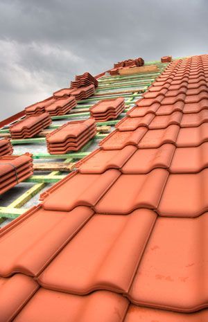 Red roof tiles being installed on a steep roof under cloudy sky