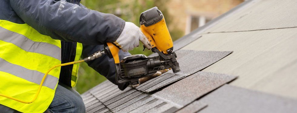 Worker using a yellow nail gun to install roof shingles on a rooftop