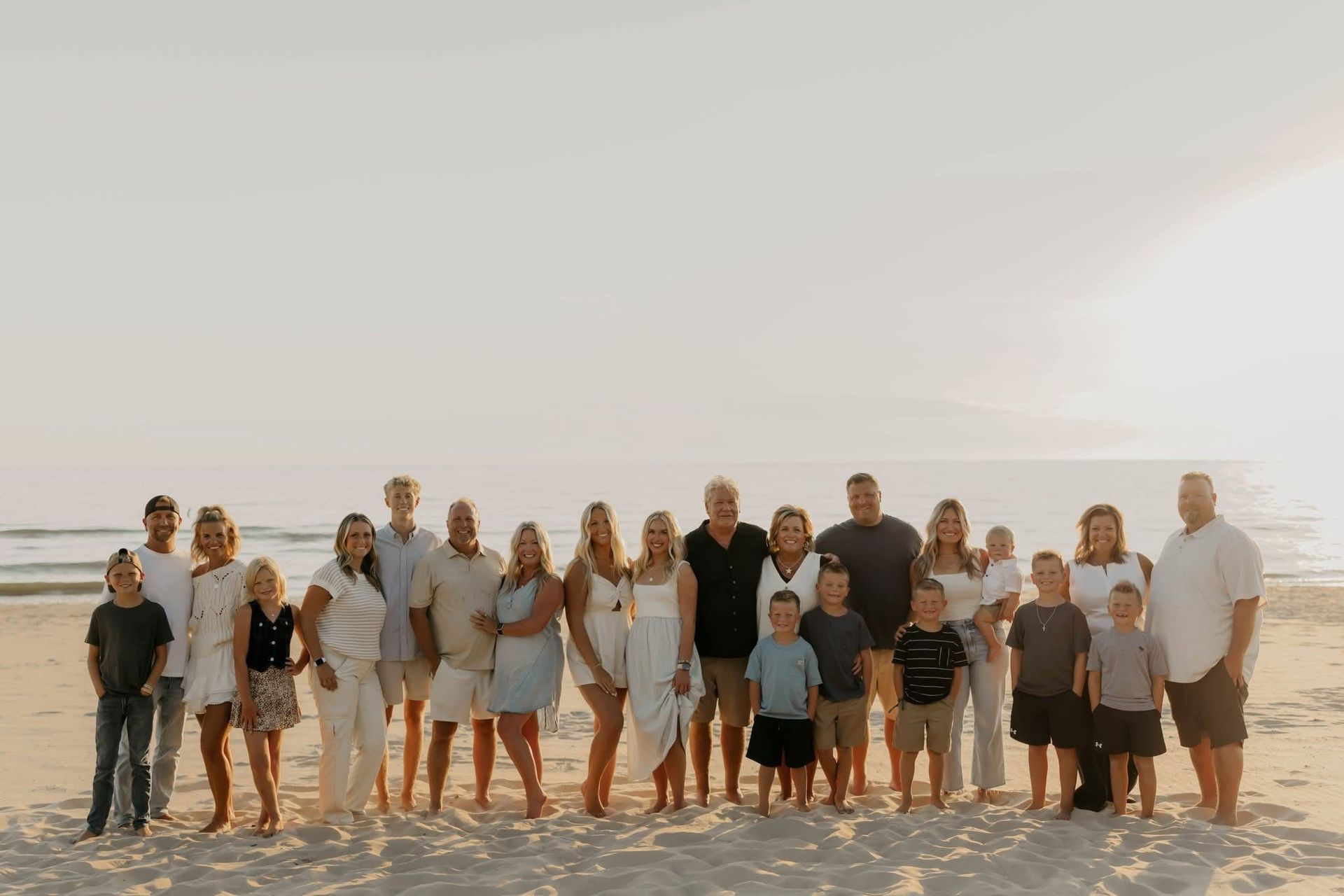 Large group standing on a sandy beach at sunset, posing for a photo by the ocean