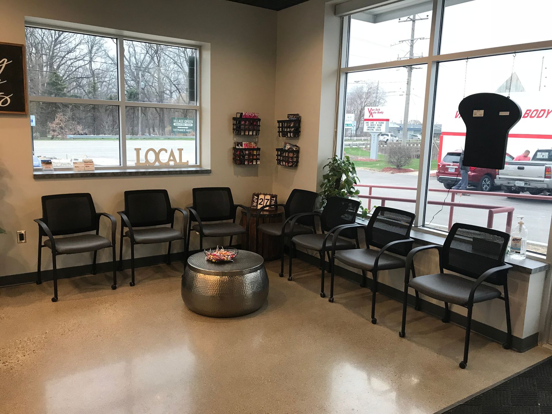 Waiting area with black chairs, large windows, and a silver ottoman in a storefront lobby.