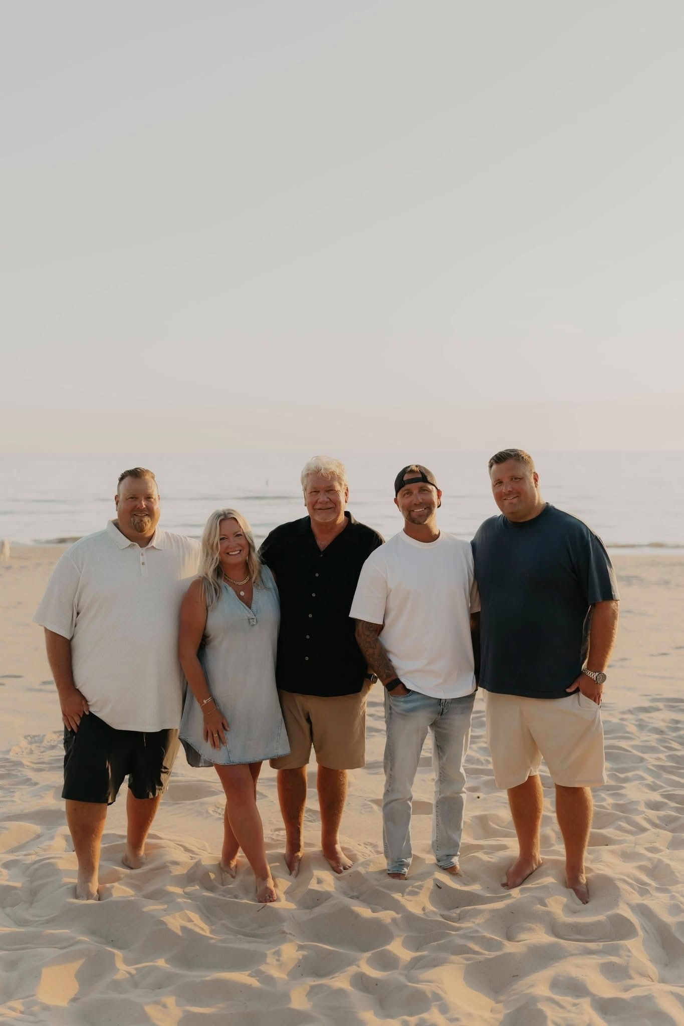 Four people standing on a sandy beach at sunset, facing the camera.