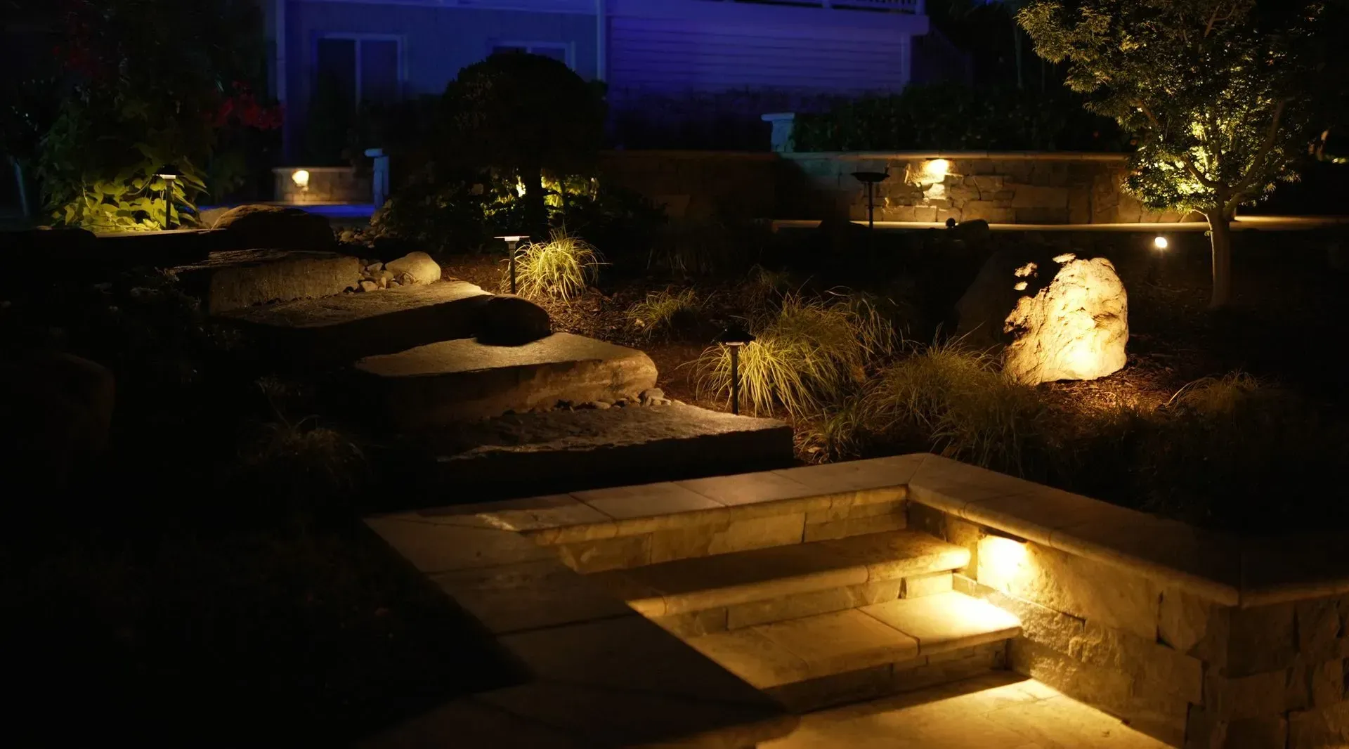Stone staircase with landscape lighting illuminating steps, rocks, and plants at night