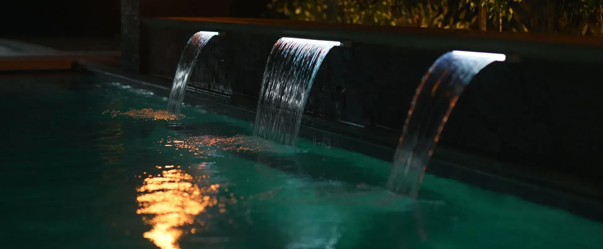 Waterfalls cascade into a teal-colored pool at night