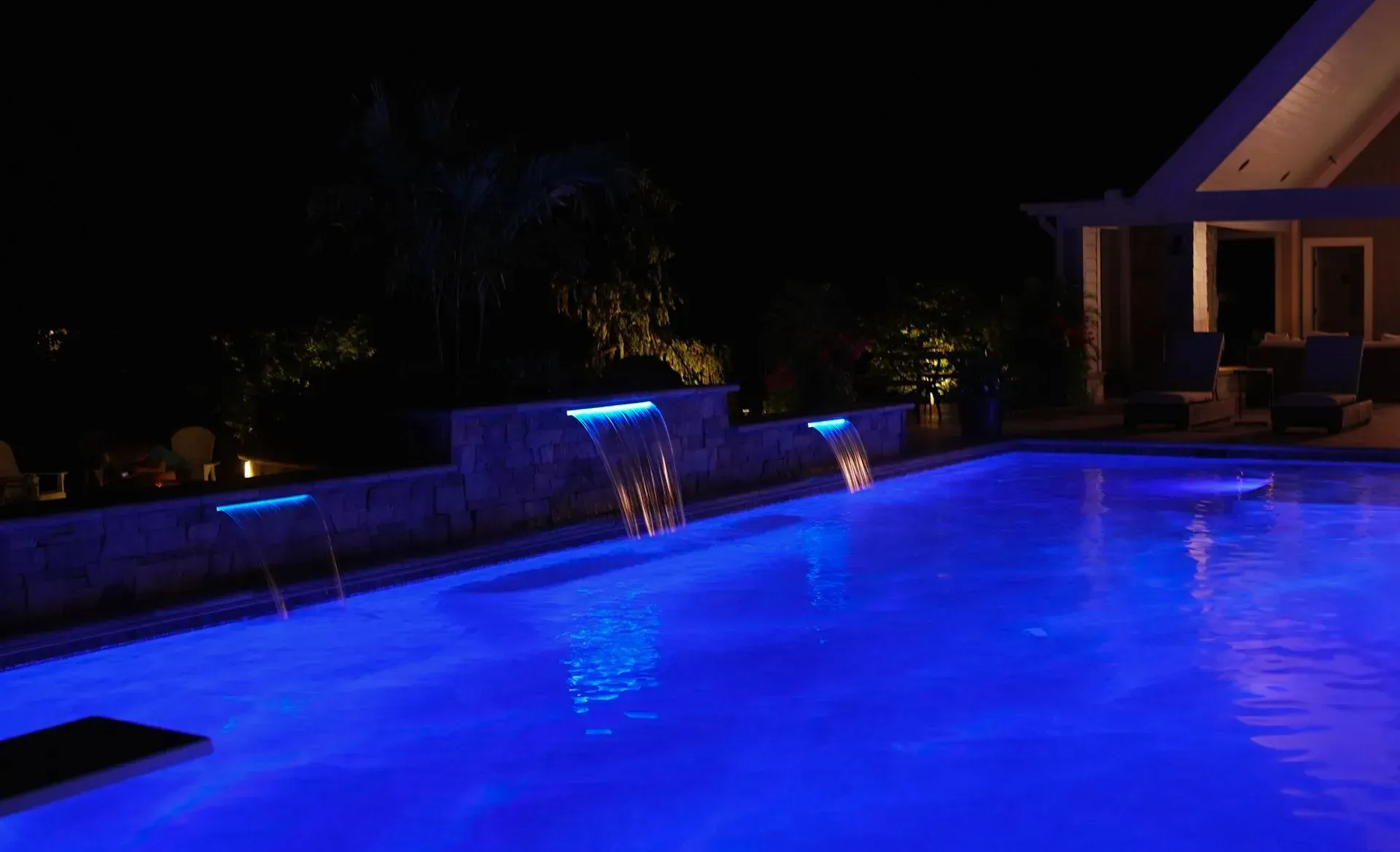 A nighttime pool with illuminated blue water and three waterfalls against a dark background