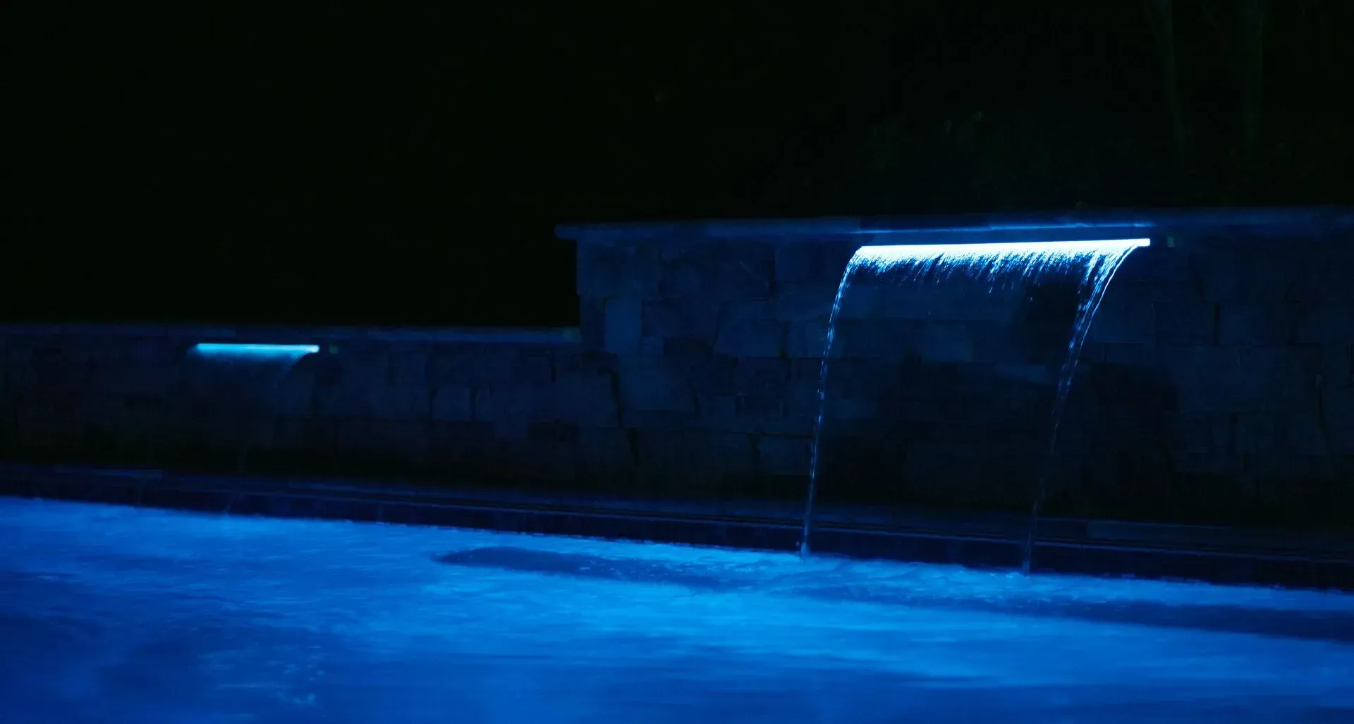 Blue-lit waterfall cascading into a pool at night