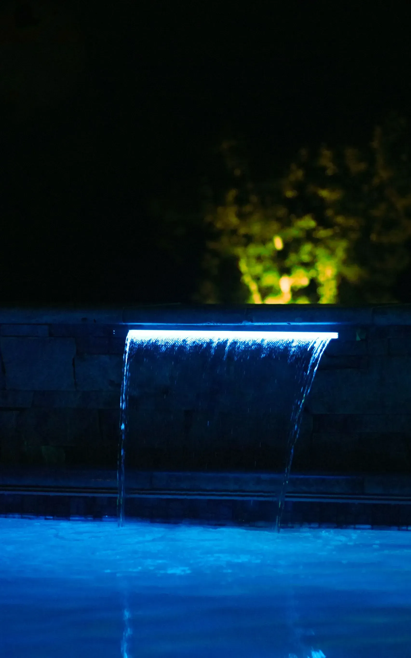 Blue-lit waterfall cascading into a pool at night