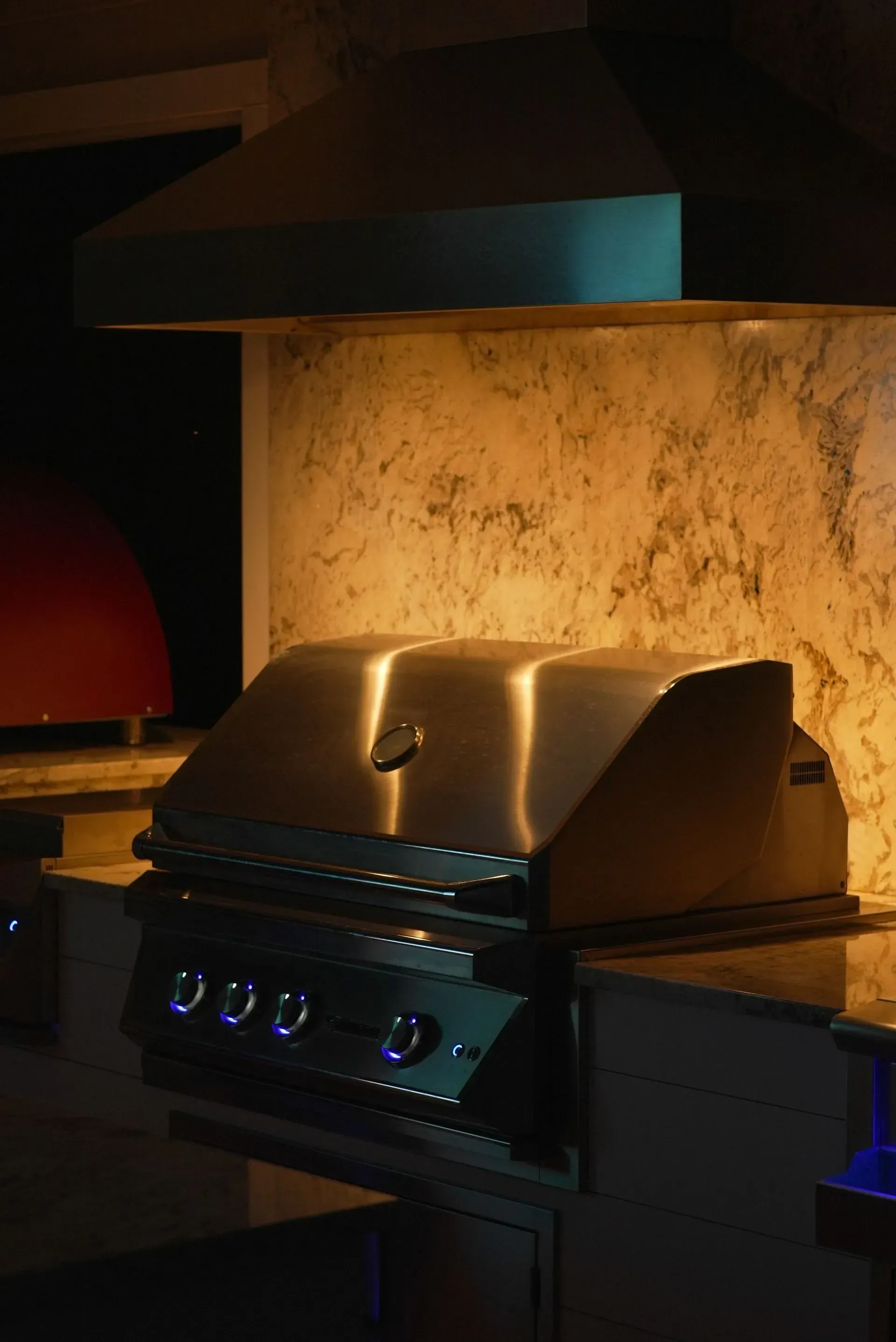 Outdoor grill with stainless steel hood, countertop, and illuminated backsplash