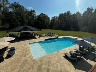a large swimming pool surrounded by chairs and umbrellas in a backyard