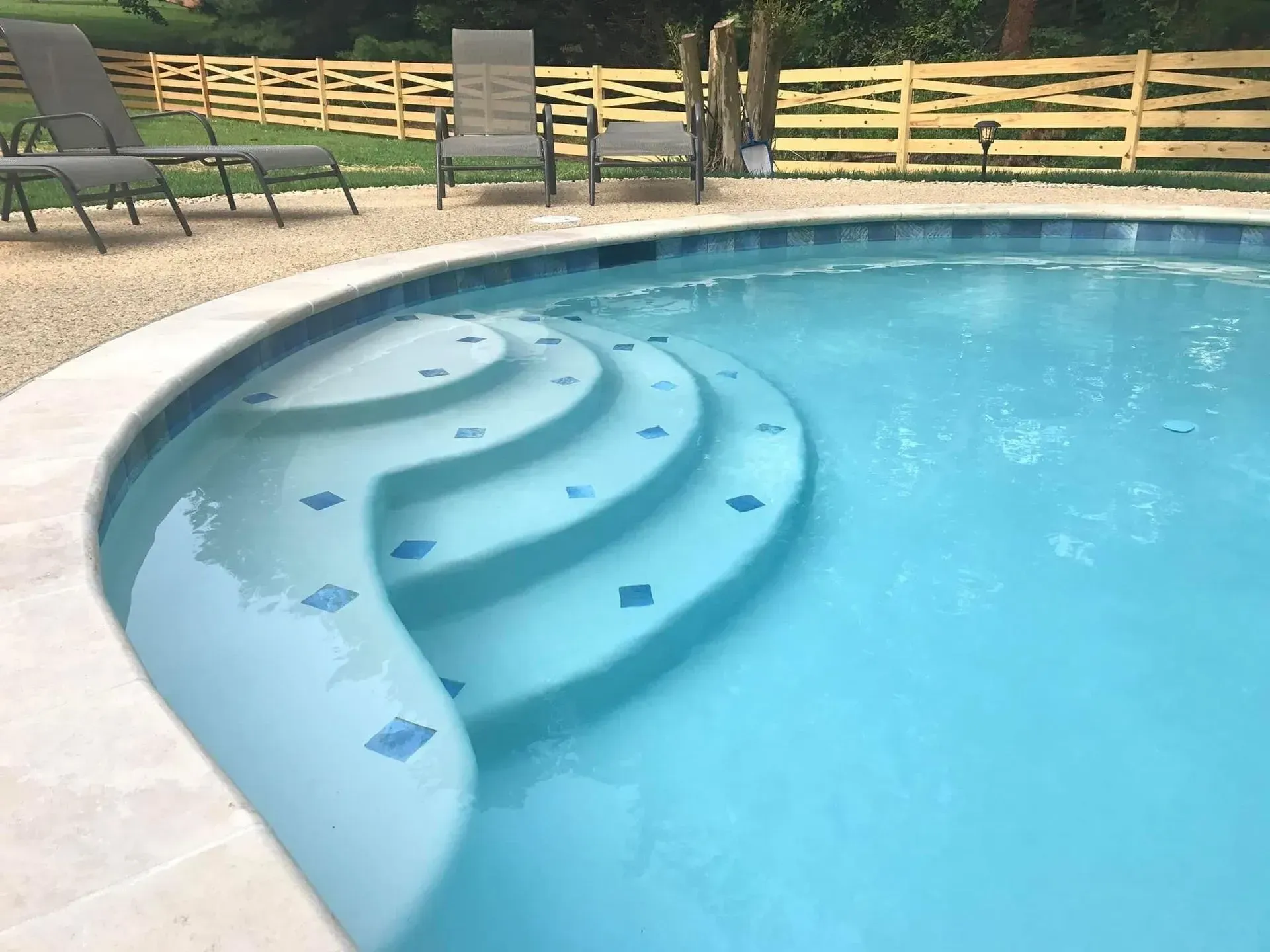 a swimming pool with stairs and chairs in the background