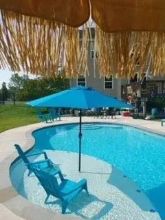 a large swimming pool with a blue umbrella and chairs