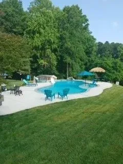 a large swimming pool surrounded by chairs and umbrellas in a backyard