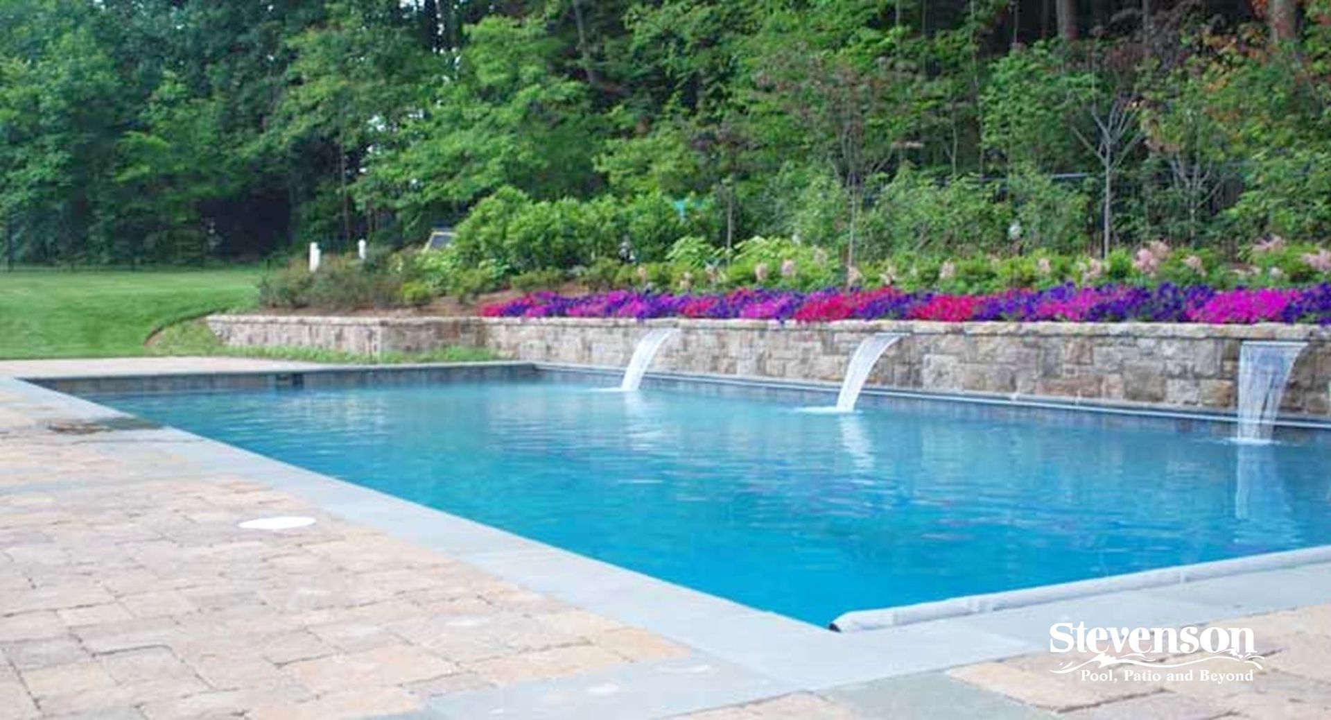 A large swimming pool with a waterfall and flowers in the background.