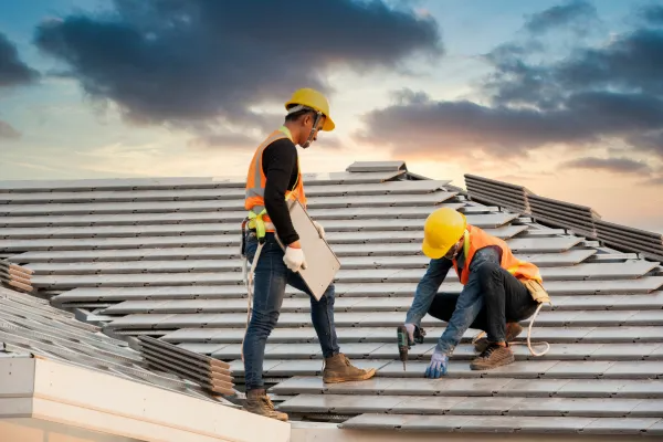 Two workers in hard hats repairing a metal roof at sunset
