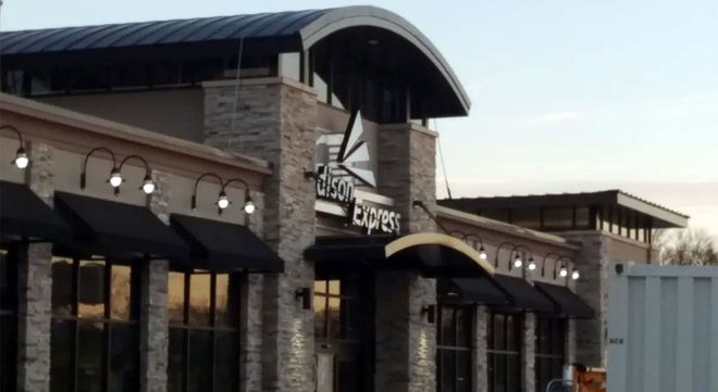 Stone and metal storefront with arched awnings and string lights on a commercial building exterior.