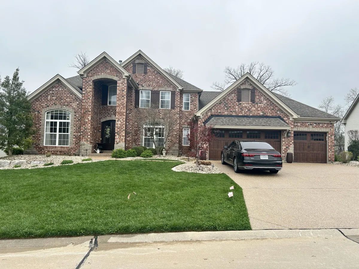 Brick suburban house with two garages, a parked SUV, and a manicured front lawn