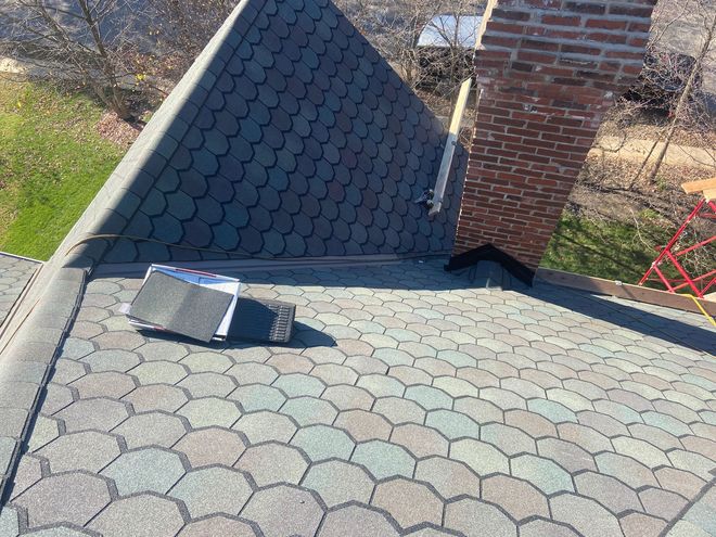 Shingled roof with a small skylight and a brick chimney on the right.