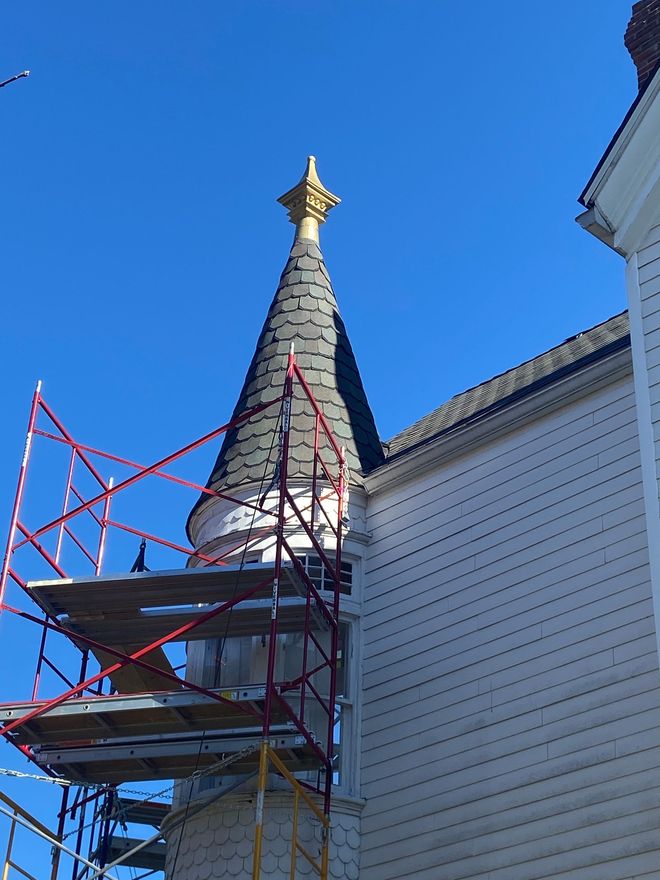 Red scaffolding beside a white building with a tall gray steeple against a blue sky.