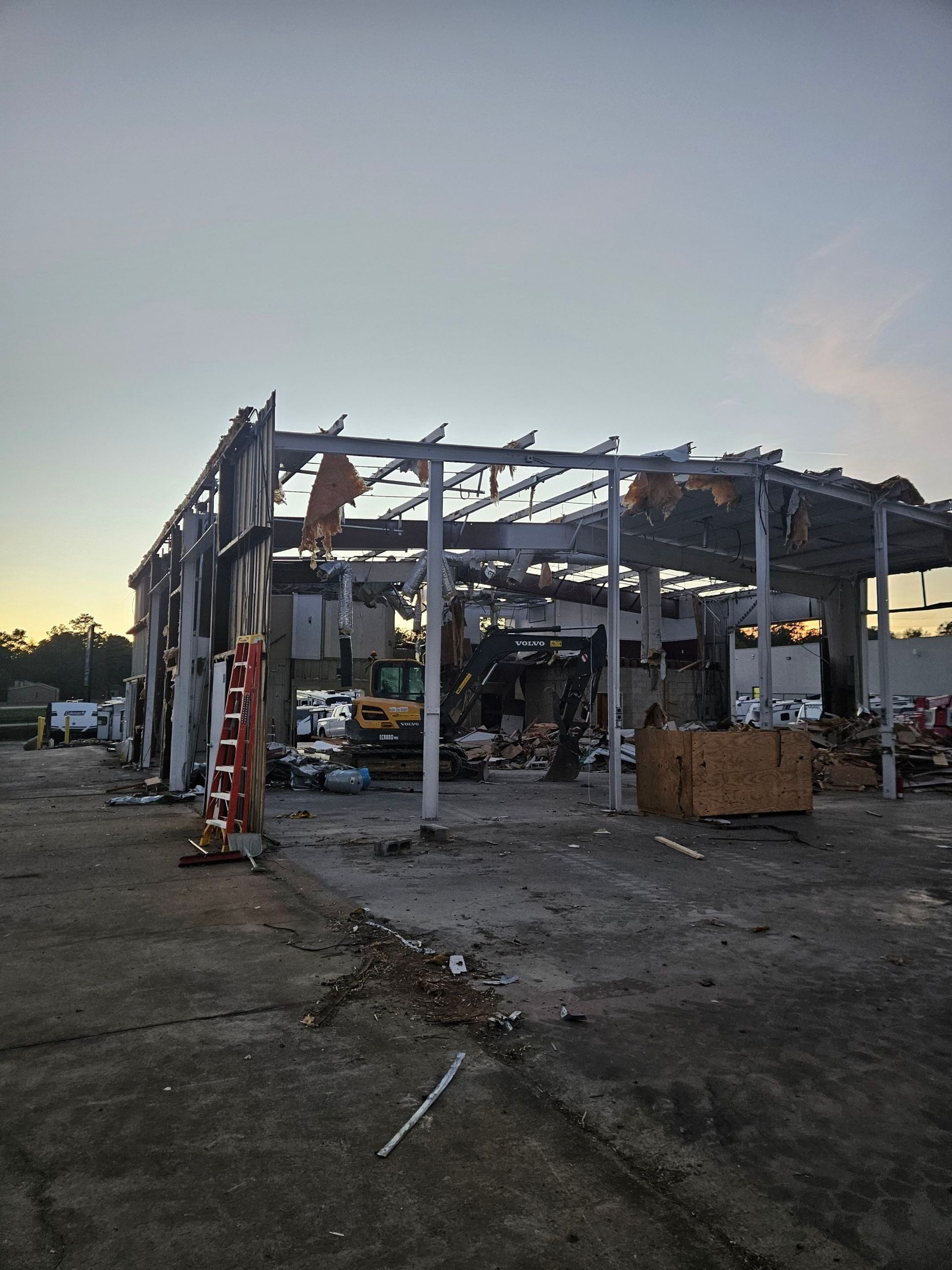 Partially demolished building frame at dusk, with debris and construction equipment inside.