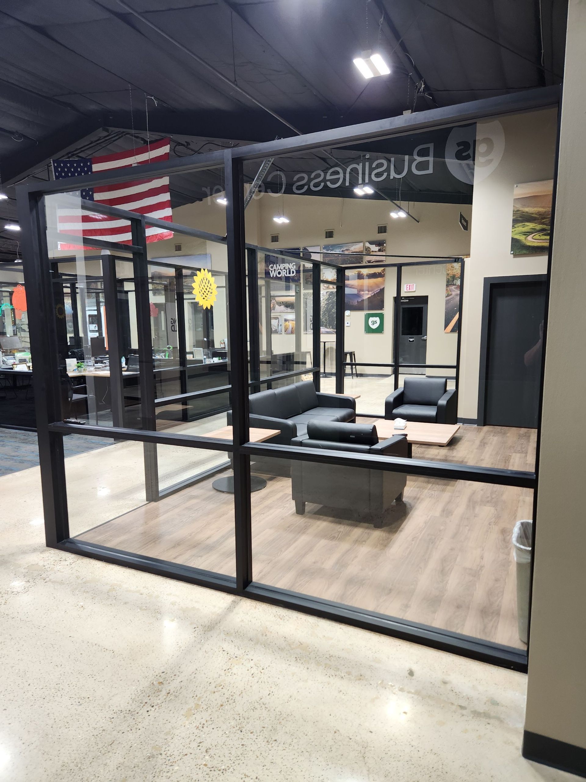 Glass-walled office or storefront interior with desks and a large American flag mural inside.