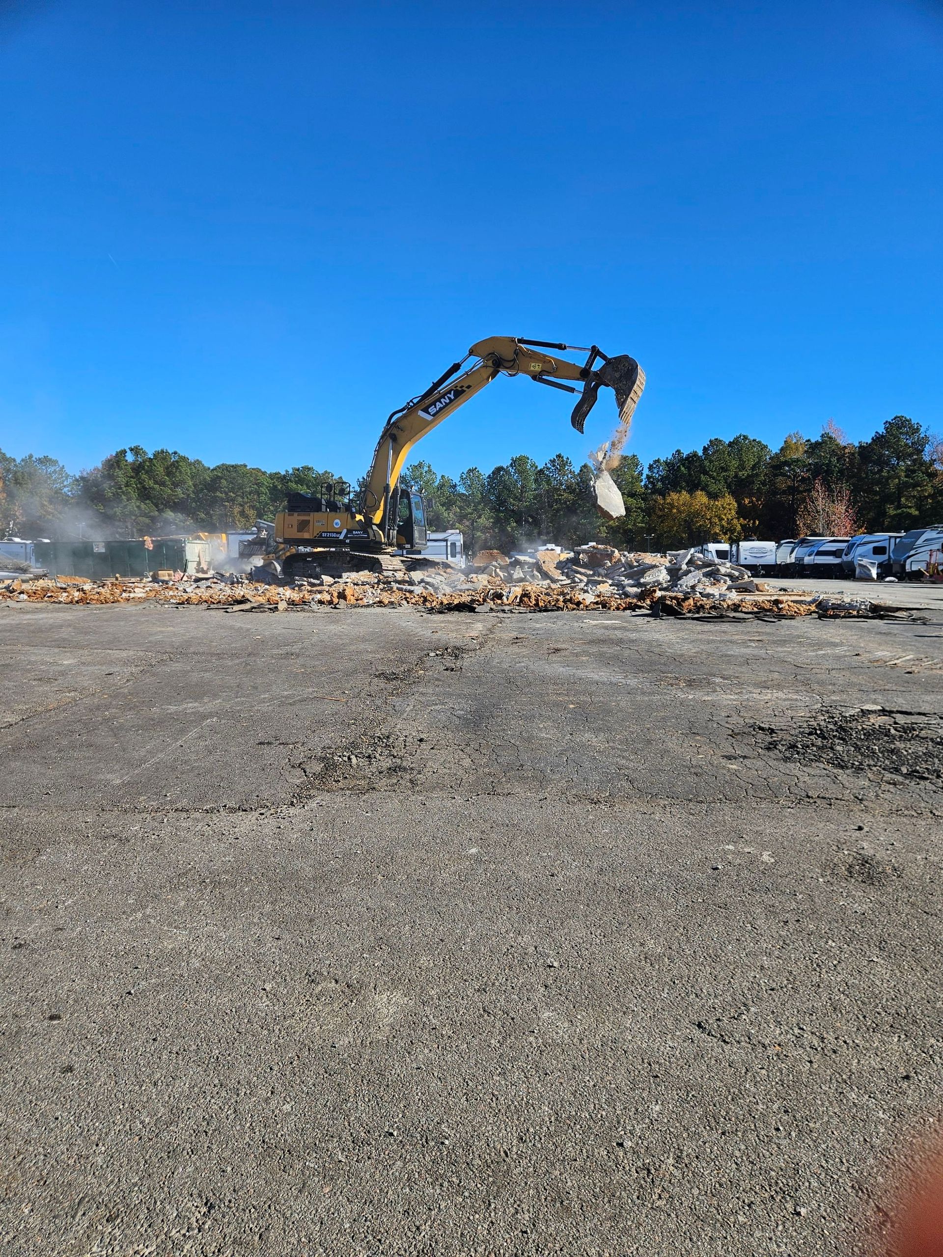 Excavator demolishing debris on a construction site under a clear blue sky