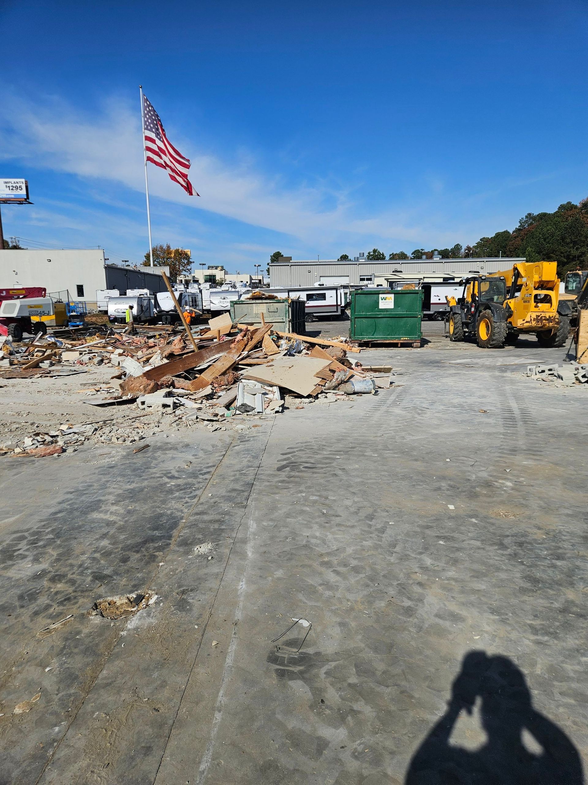 Construction site with rubble piles, yellow equipment, and an American flag under a blue sky