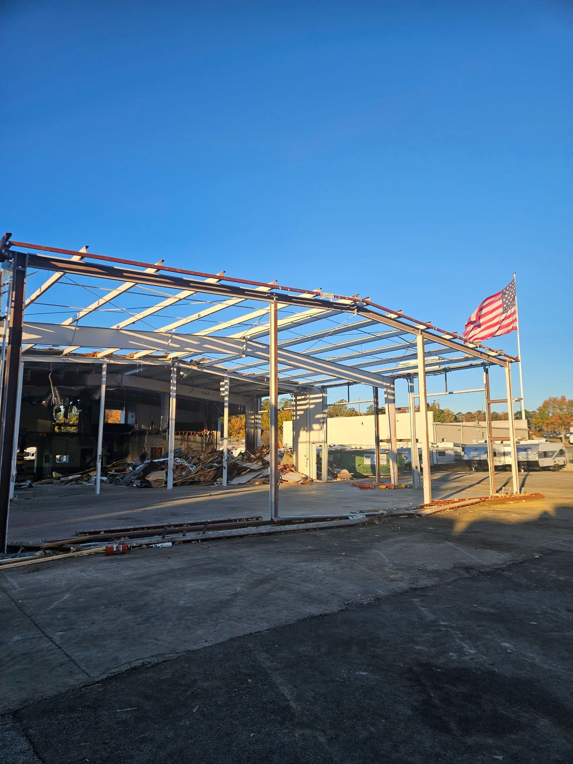 Partially destroyed building with exposed beams and an American flag under a clear blue sky