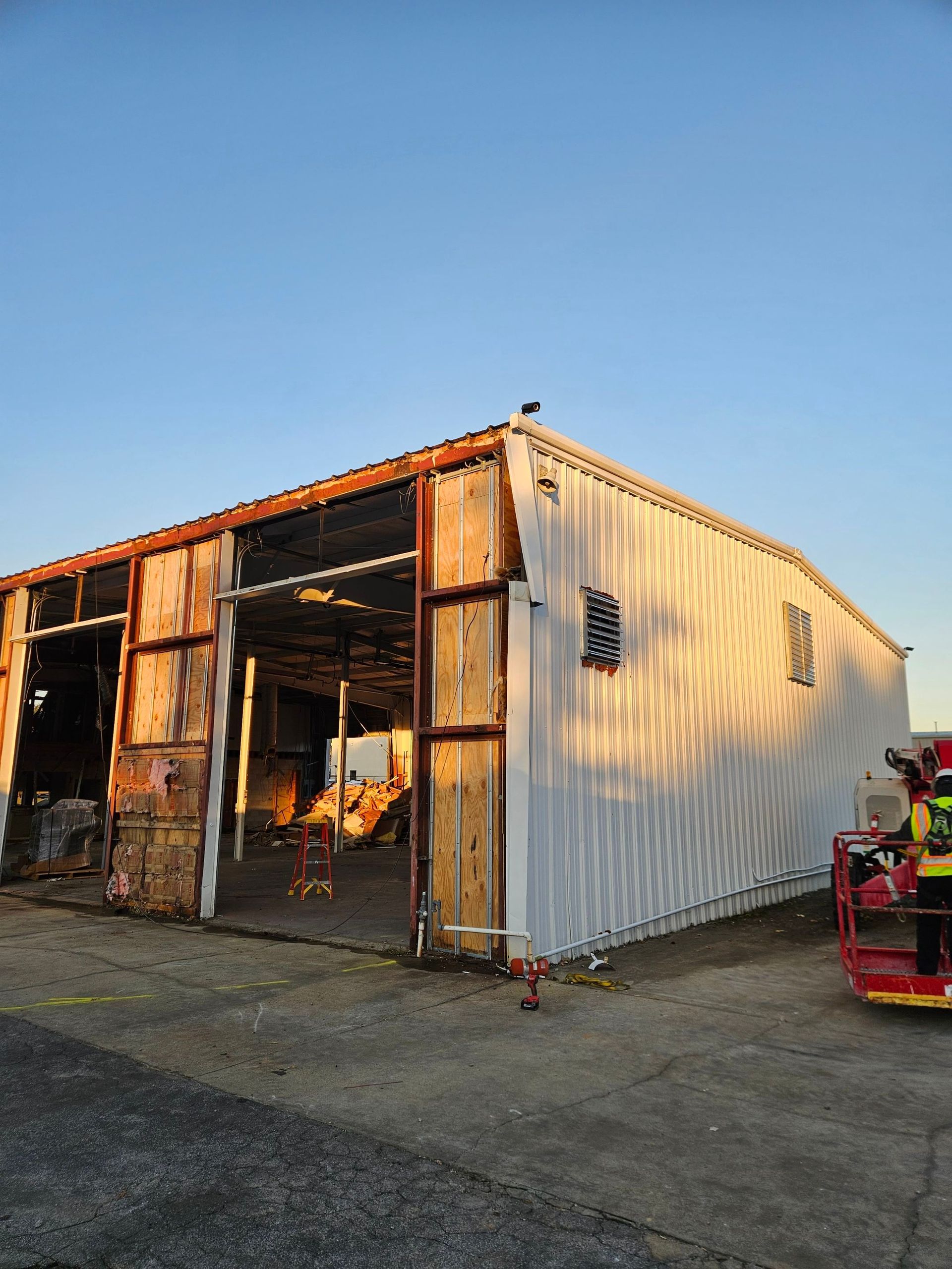 Rustic metal shed with open bay doors beside a red utility vehicle at sunset