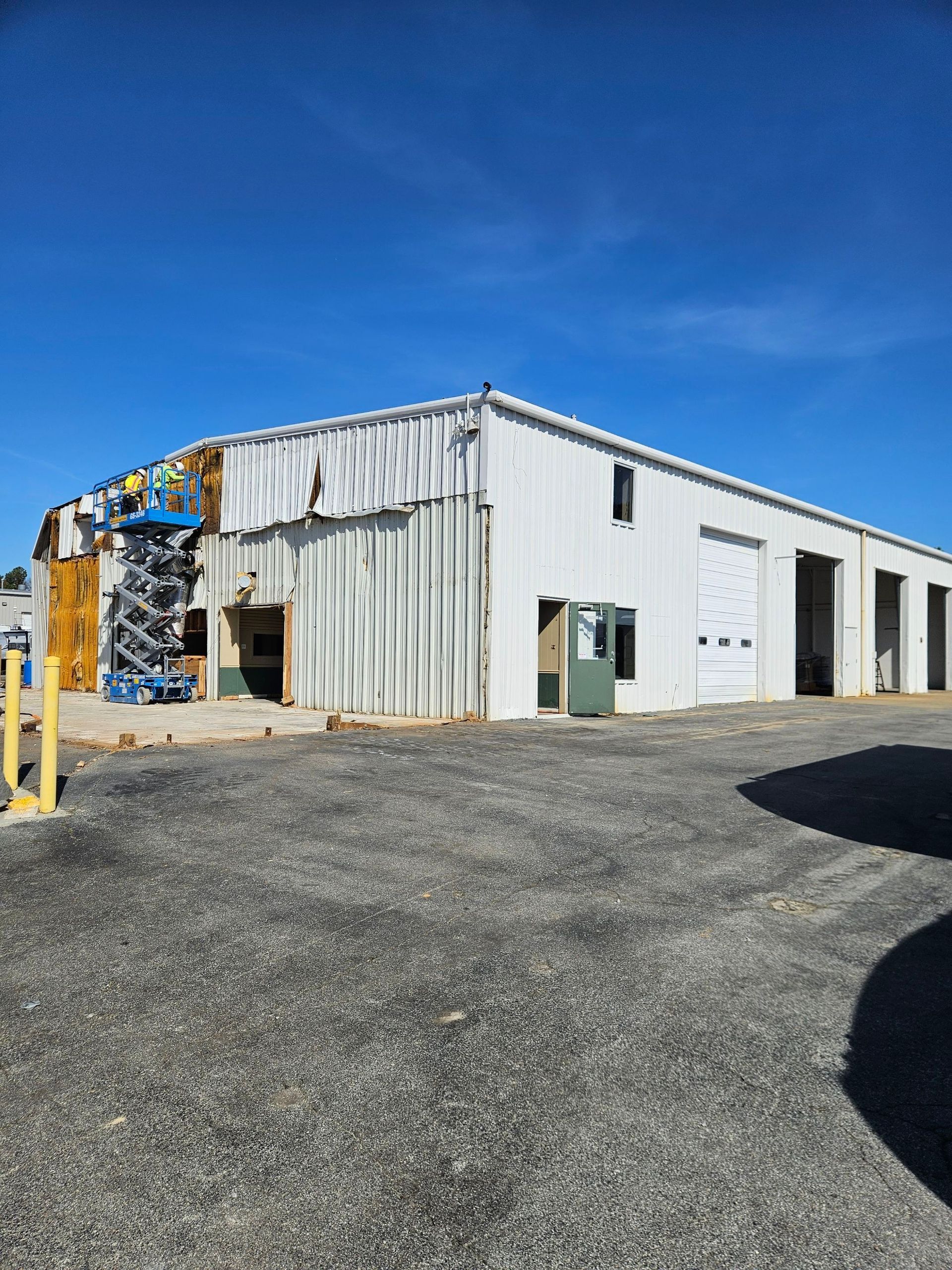 Industrial warehouse with corrugated metal siding, gravel lot, and stacked recycling materials under a blue sky