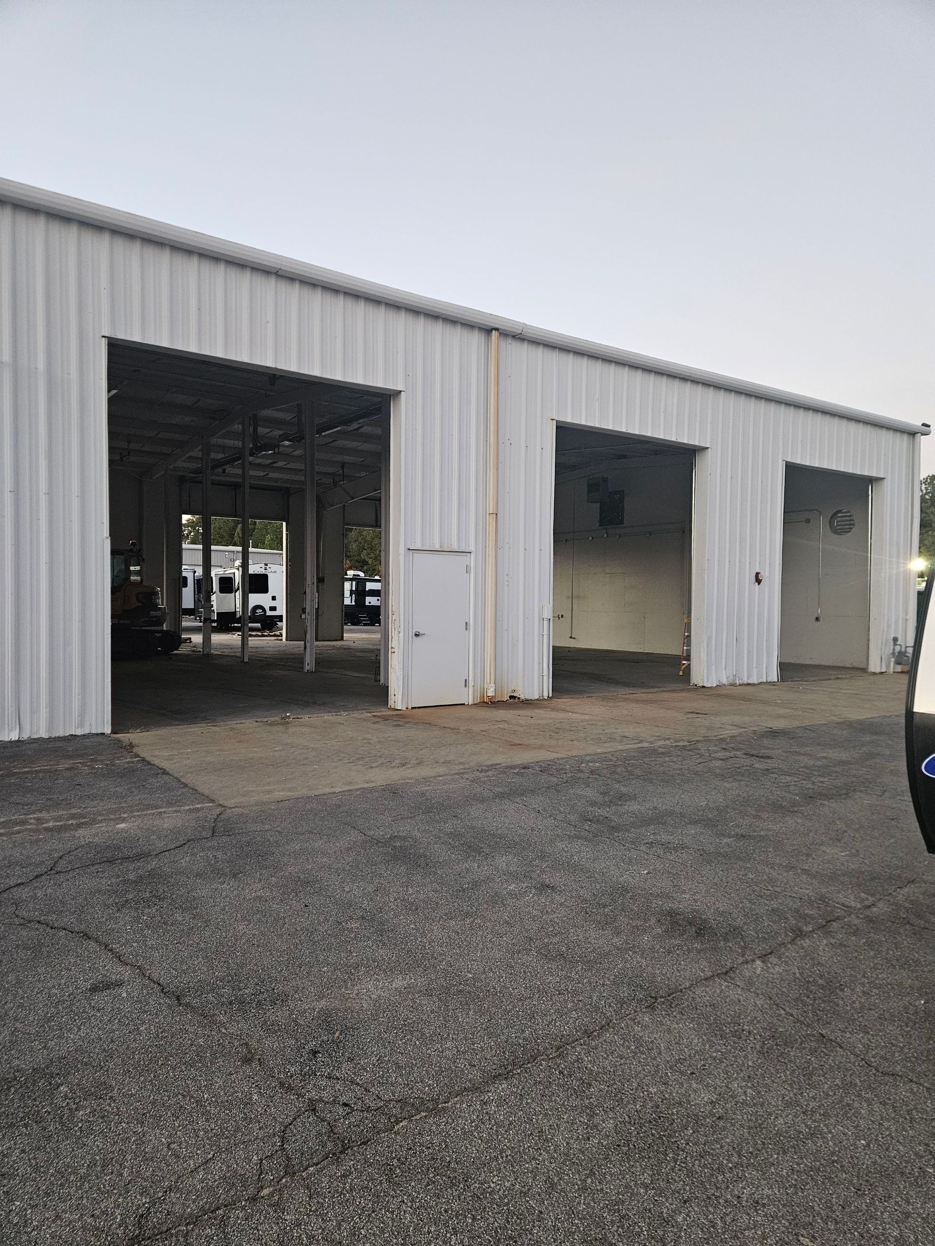 White metal industrial building with open garage bays on a gravel lot under an overcast sky
