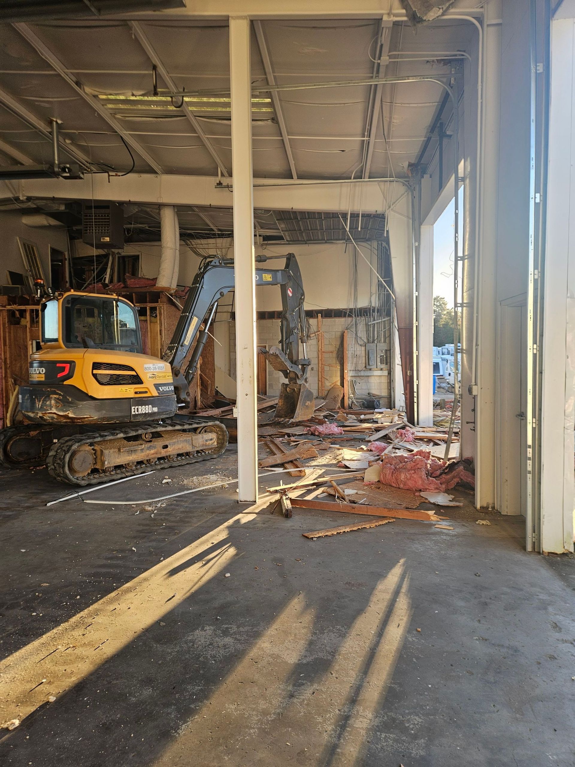 Damaged building interior with debris, an excavator, and broken columns under a collapsed ceiling