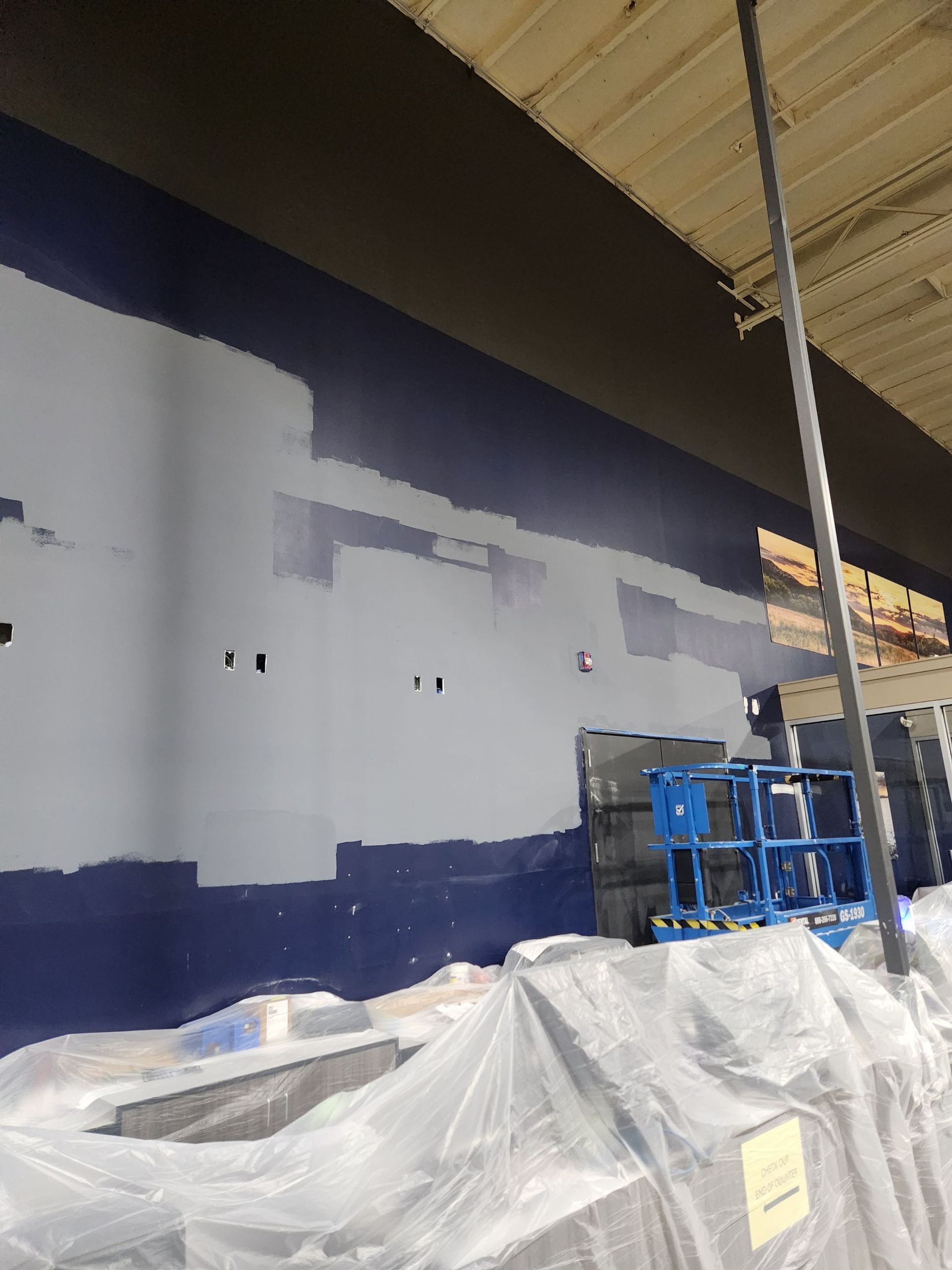 Partially painted warehouse wall in navy and white, with covered materials and stacked blue crates below a roof overhang