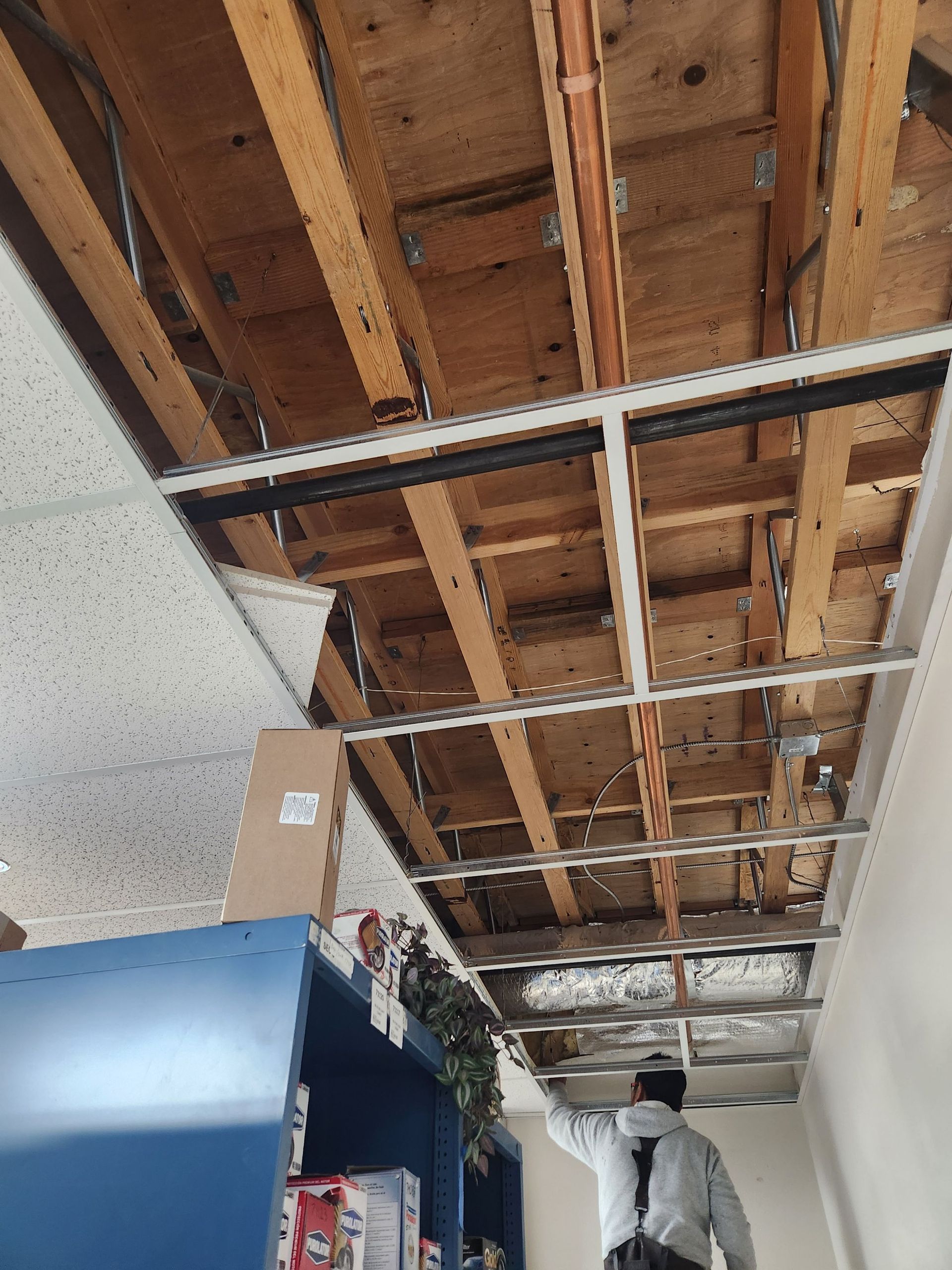 Exposed ceiling with wooden beams and a worker on a lift in an industrial room
