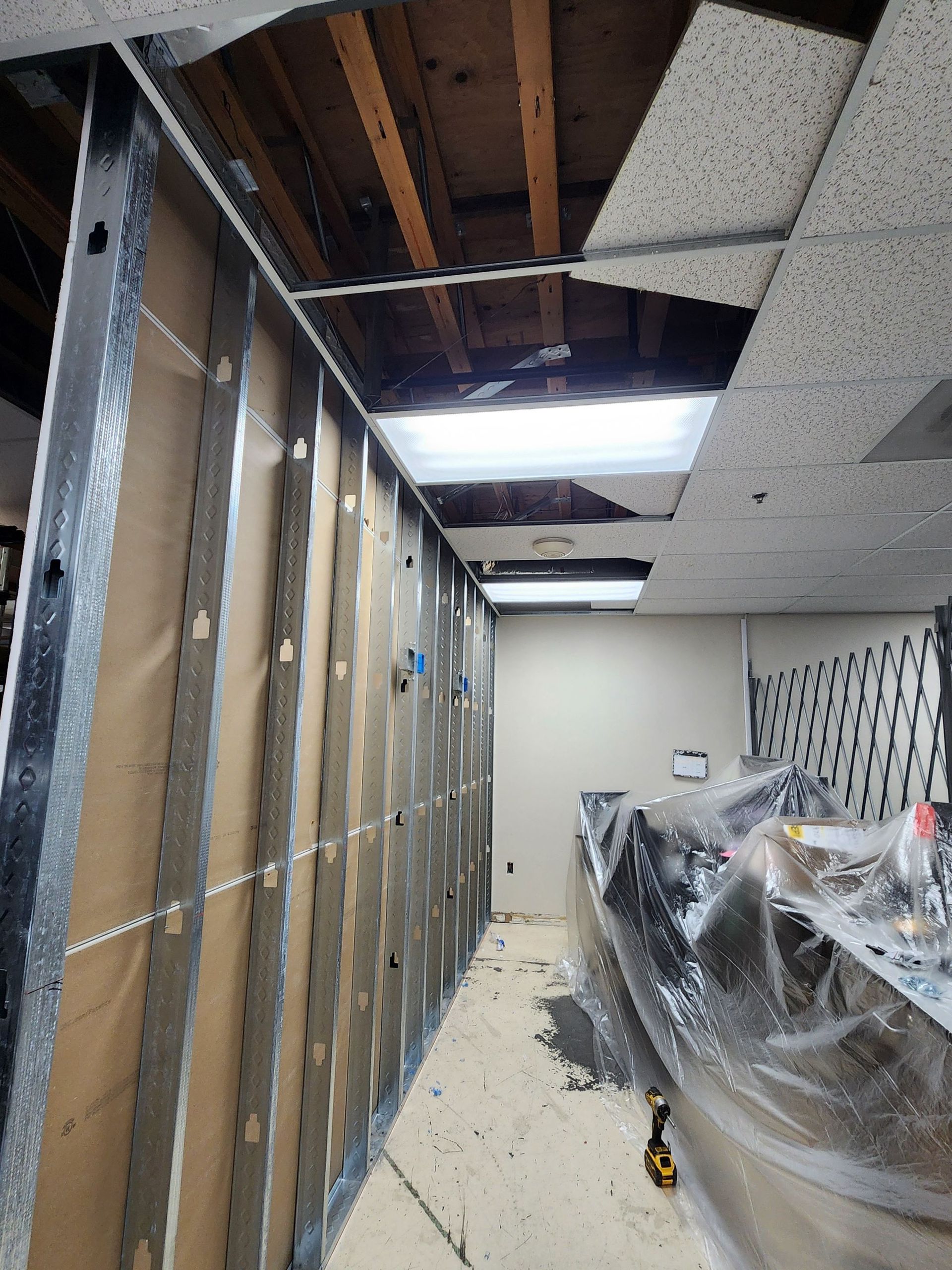 Office under renovation with exposed ceiling, unfinished walls, and covered furniture.