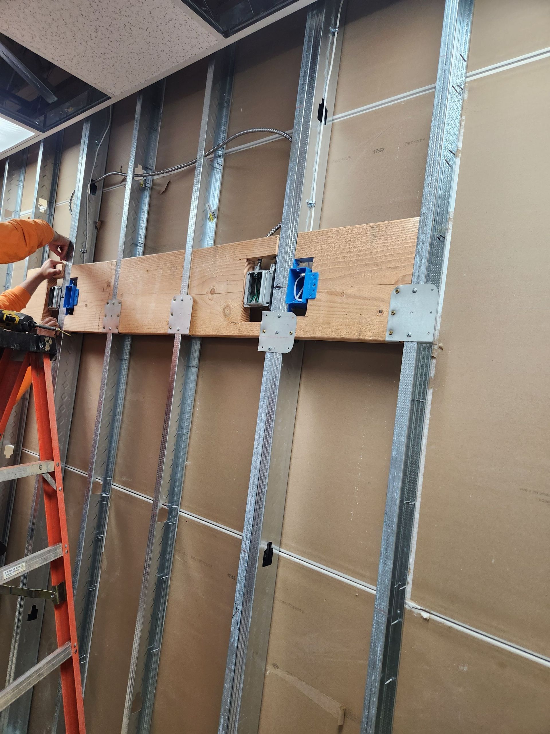 Worker fastening cardboard to metal wall studs with blue clamps during construction