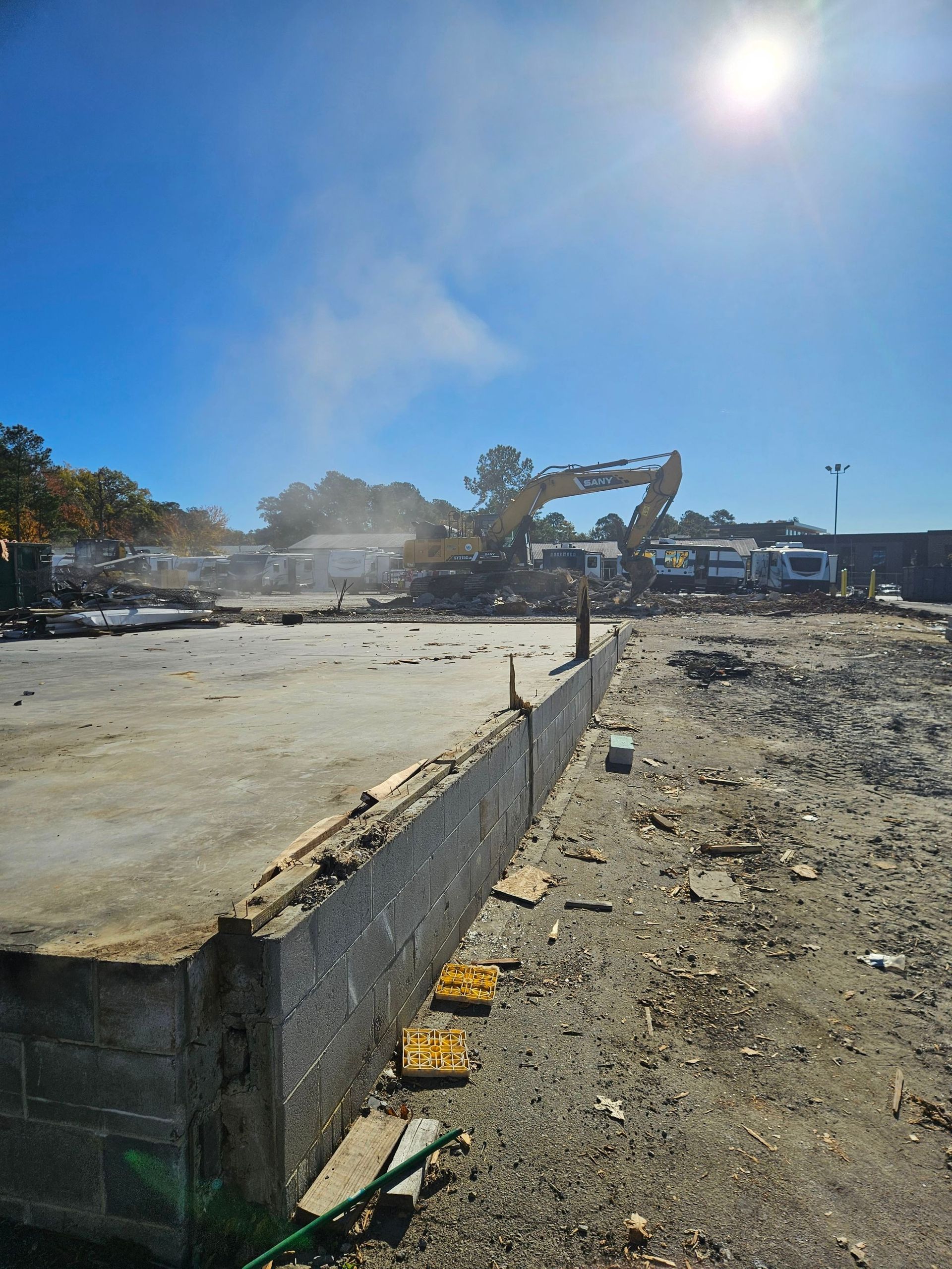 Demolition site with excavator dust, broken concrete, and rubble under a bright blue sky