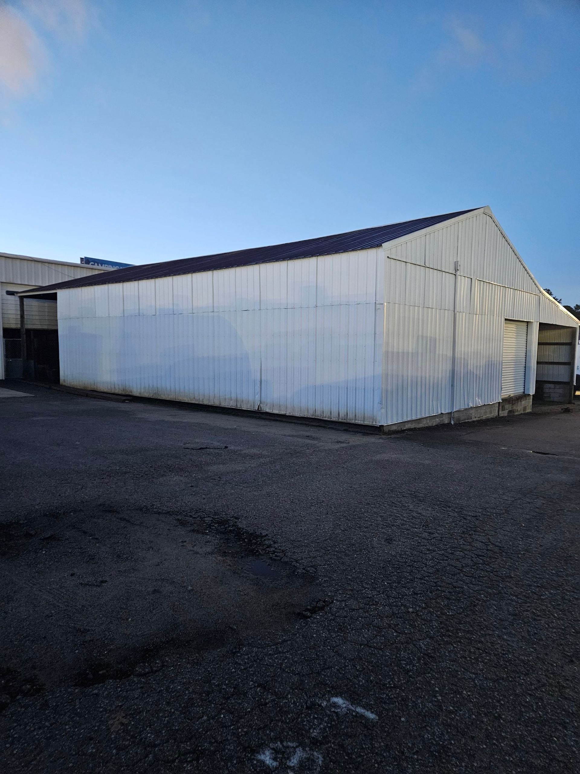 White corrugated metal warehouse building on an empty asphalt lot under a blue sky