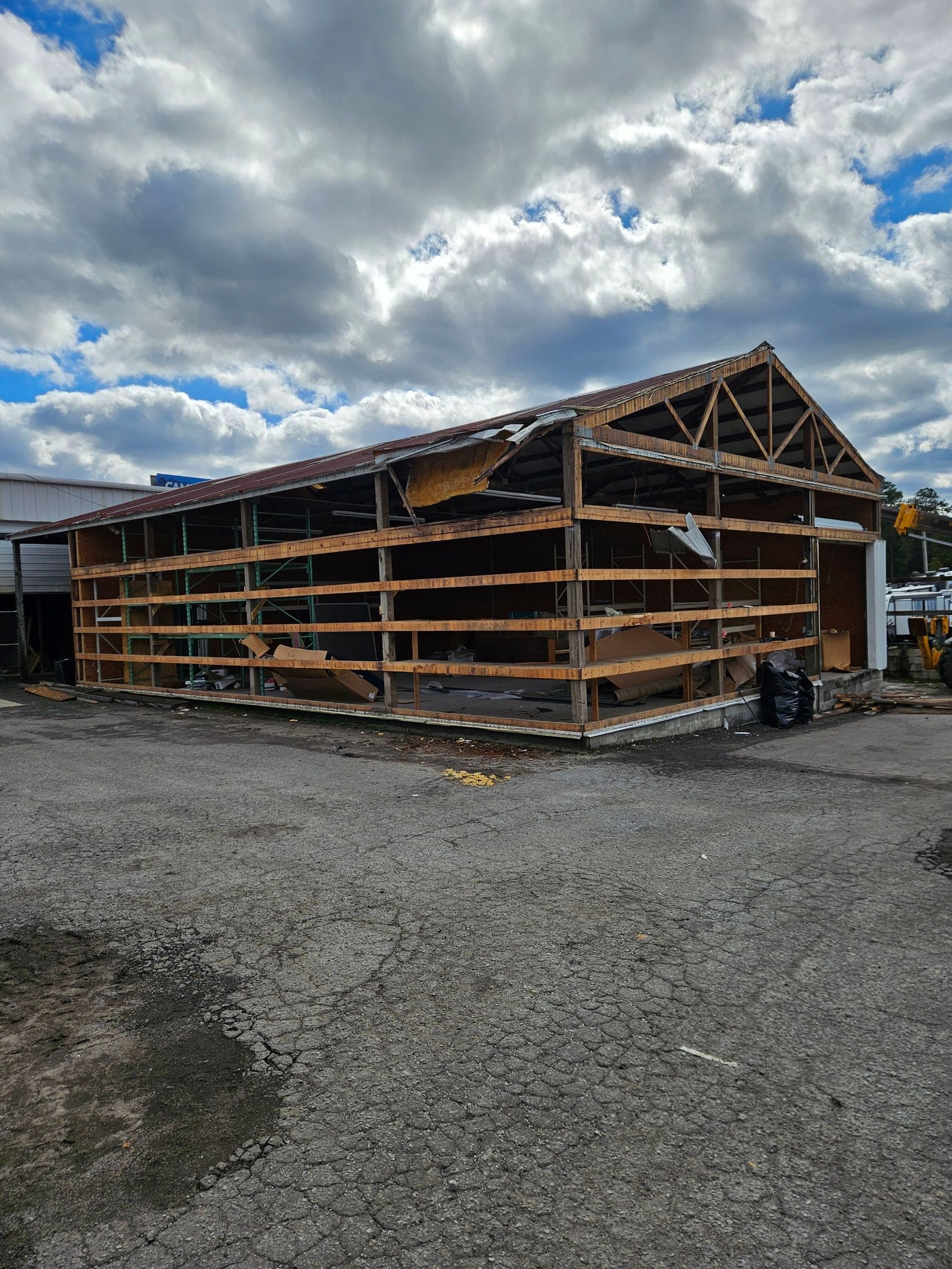 Partially demolished wooden building under a cloudy sky, surrounded by gravel.