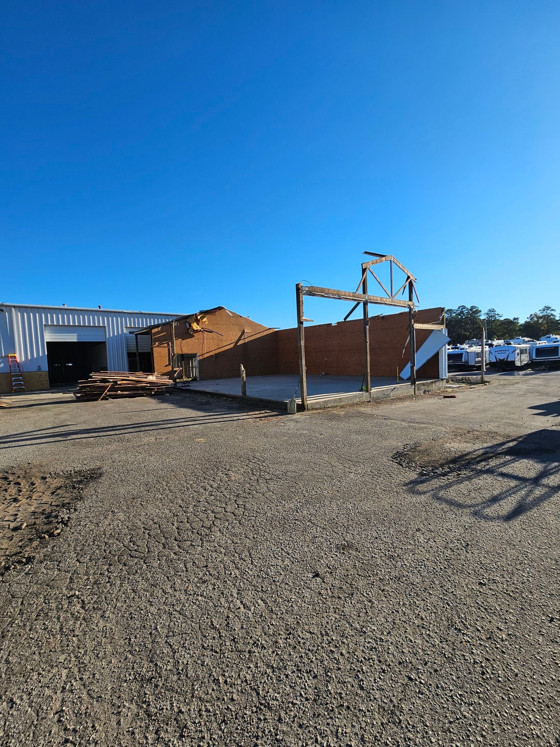 Gravel lot with a brown building frame under construction beside white tents and blue sky