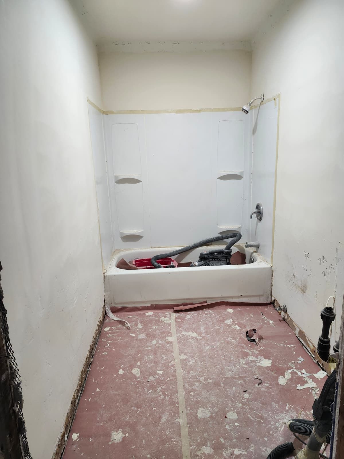 Narrow unfinished bathroom with a built-in tub, peeling paint, and construction debris on the floor.