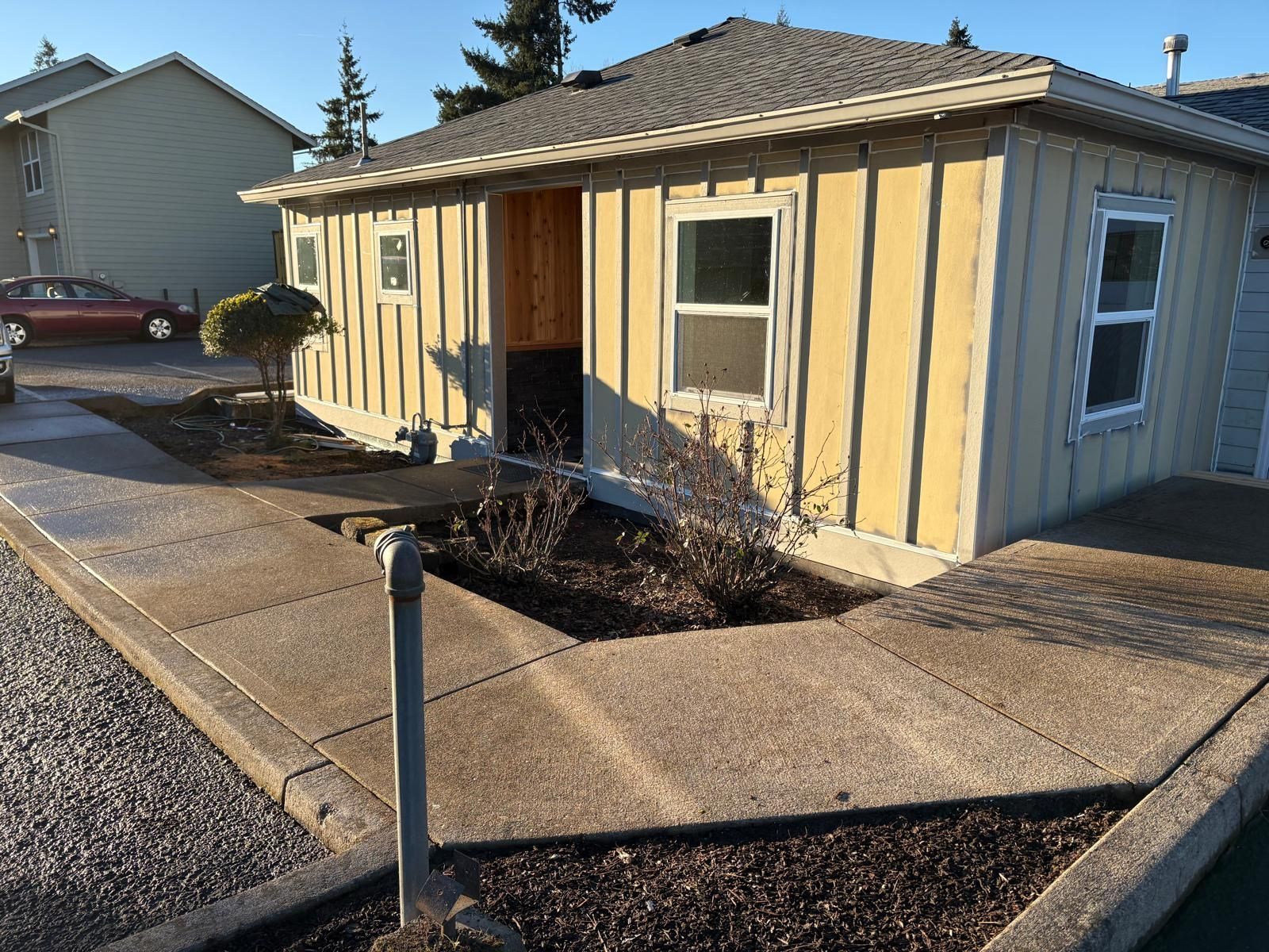 Small yellow house with a front porch and leafless shrubs beside a wet concrete walkway