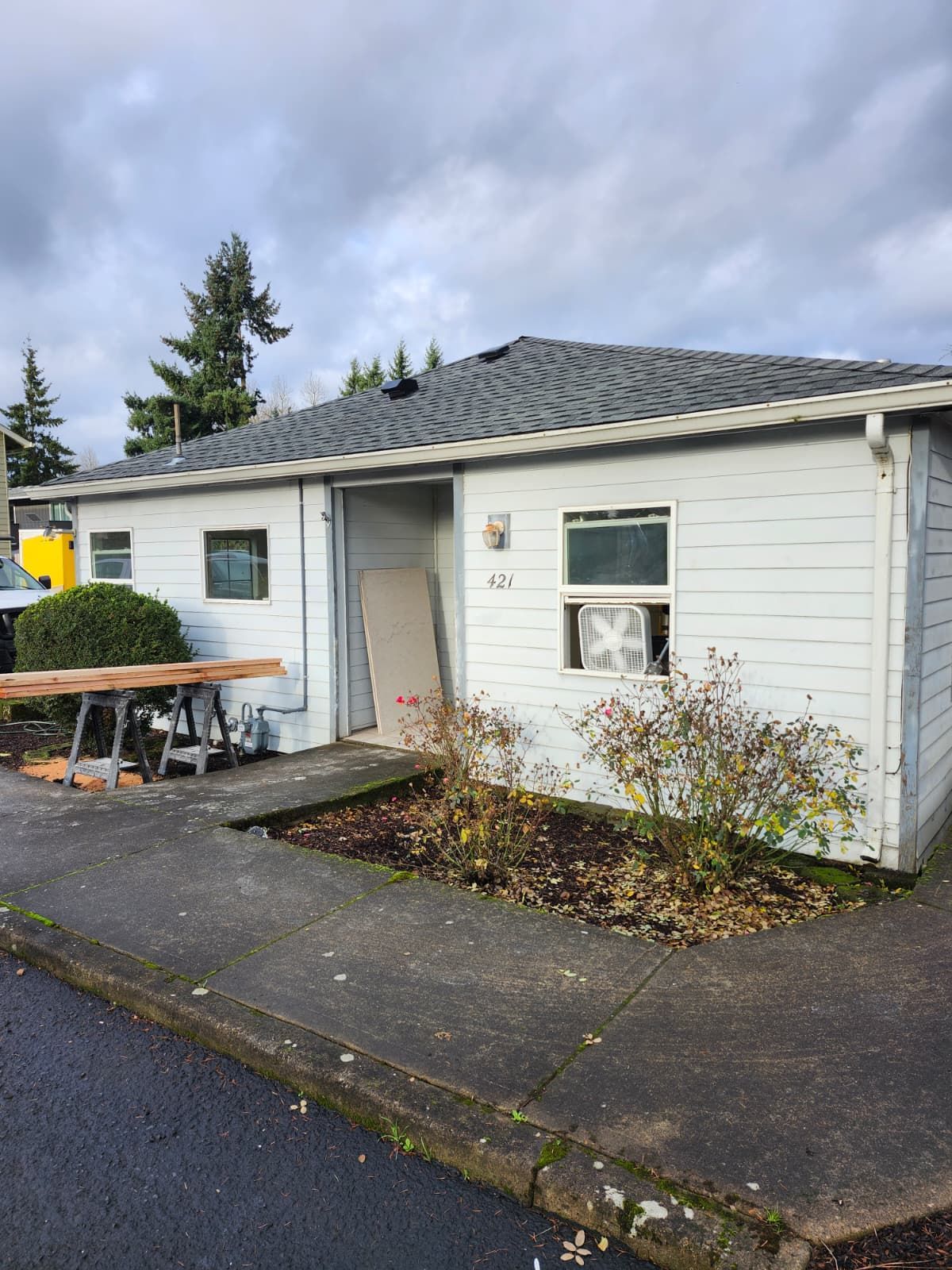 Small white house with a gray roof, front steps, and wet pavement on a cloudy day