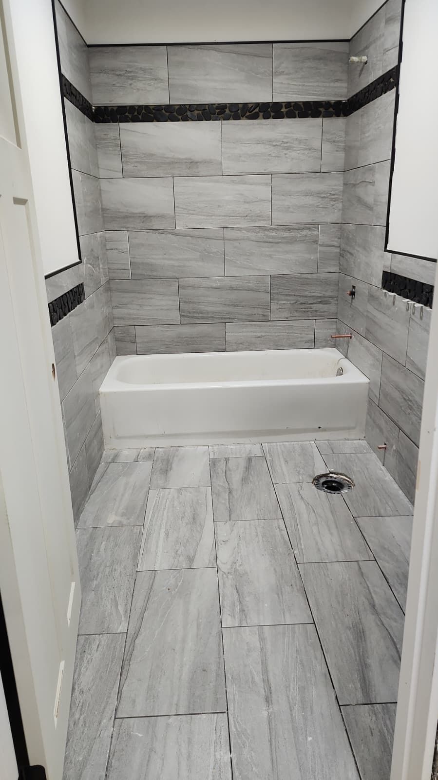 Small tiled bathroom with a white tub/shower alcove and gray stone-pattern walls and floor.