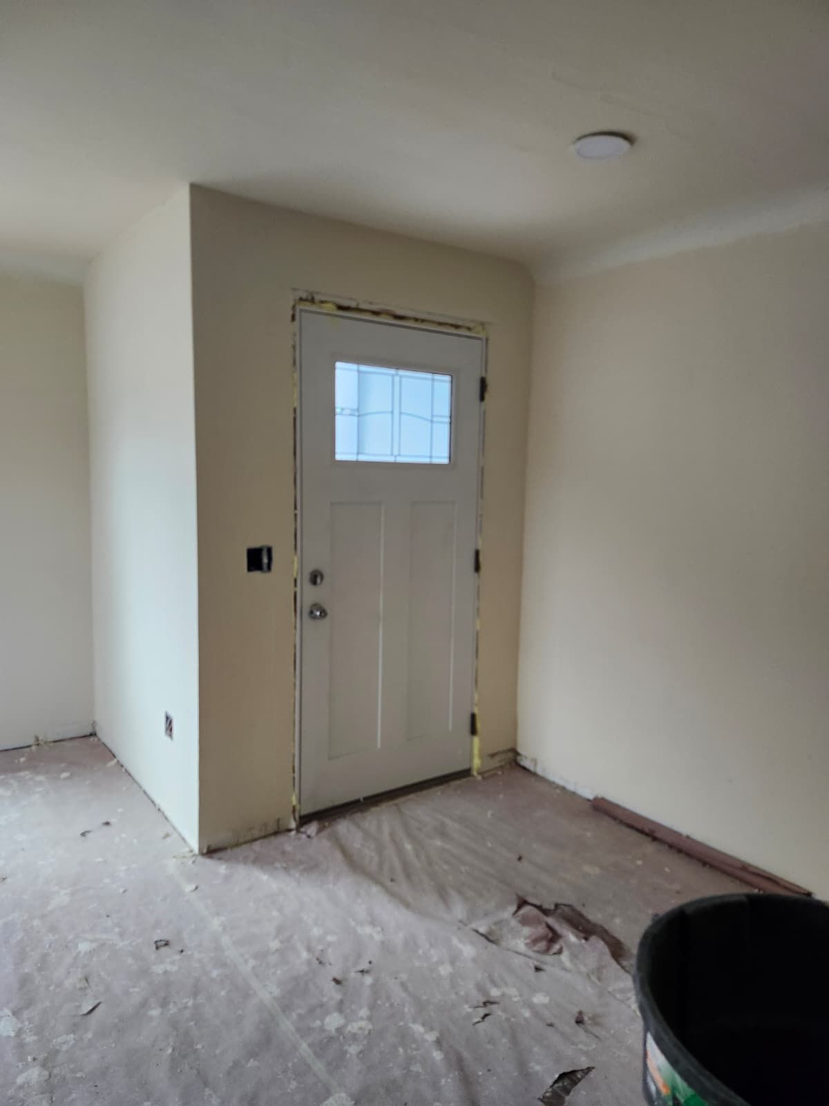 Bare interior room with a white door, unfinished floor, and beige walls.