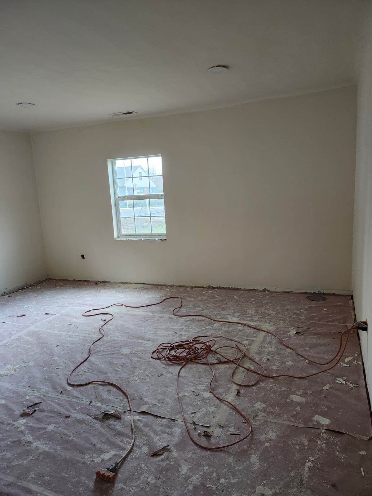 Empty room under renovation with a window and exposed wiring on the unfinished floor