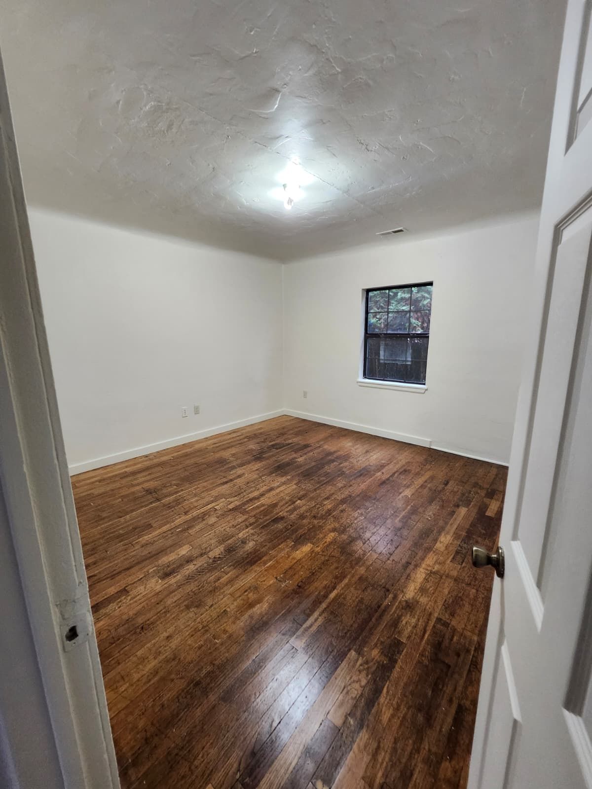 Empty white room with brown hardwood floors and a small window
